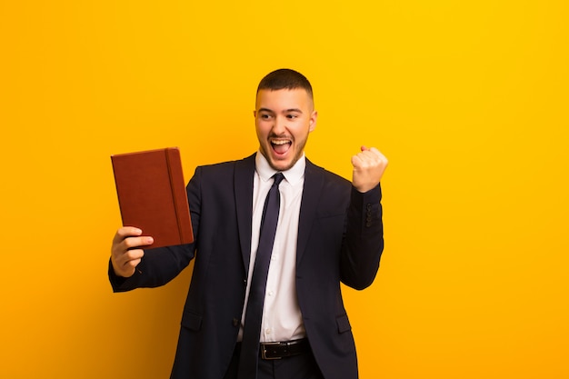 Jeune bel homme d'affaires contre un mur plat avec un livre de journal