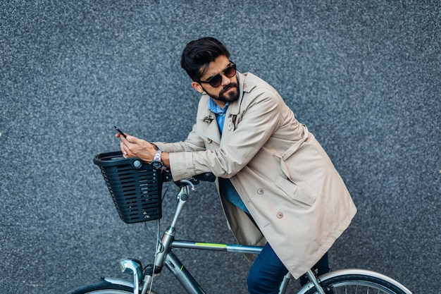 Jeune bel homme d'affaires faisant du vélo dans la rue de la ville et utilisant un téléphone intelligent. Protection de l'environnement et concept de transport écologique.