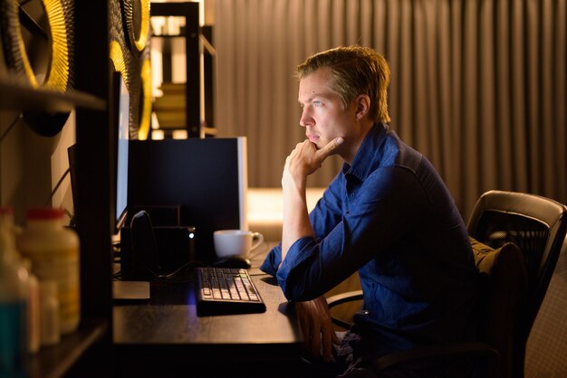 Jeune bel homme d'affaires pensant tout en travaillant des heures supplémentaires à la maison tard dans la nuit