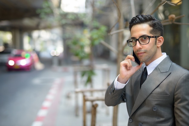 Jeune bel homme d'affaires persan, parler au téléphone dans les rues de la ville à l'extérieur