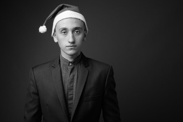 jeune bel homme d'affaires portant bonnet de Noel prêt pour Noël contre le mur gris. noir et blanc