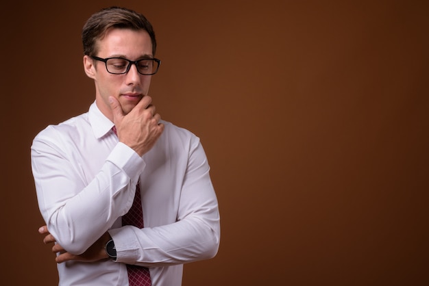 Jeune bel homme d'affaires portant des lunettes sur un mur marron