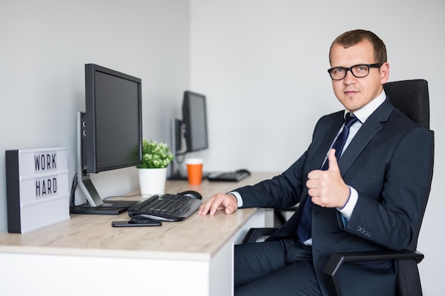 Jeune bel homme d'affaires pouce en l'air dans un bureau moderne