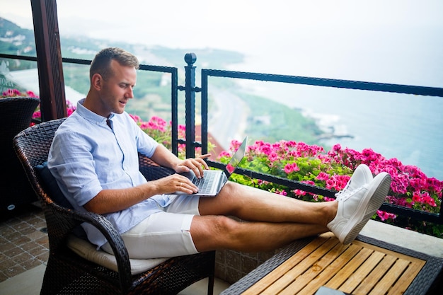 Jeune bel homme d'affaires vêtu d'une chemise blanche et d'un short est assis avec un ordinateur portable dans un café à la table. Travaillez en vous reposant. Mise au point sélective