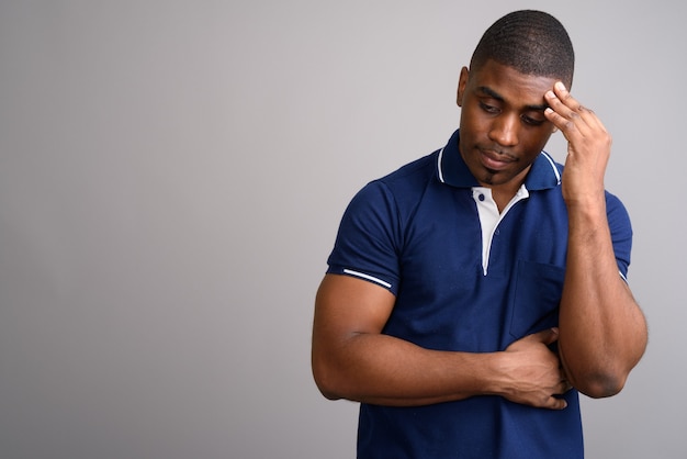 Jeune bel homme africain portant un polo bleu sur fond gris