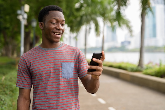 Jeune bel homme africain utilisant un téléphone mobile dans le parc