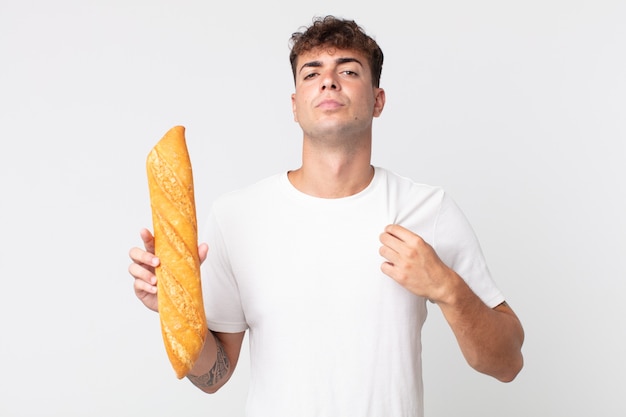 Jeune bel homme à l'air arrogant, réussi, positif et fier et tenant une baguette de pain