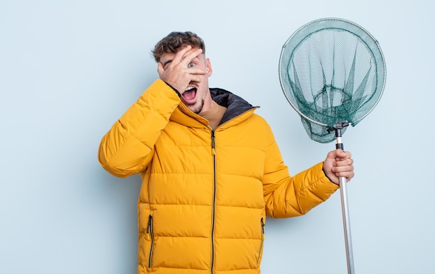 Jeune bel homme à l'air choqué, effrayé ou terrifié, couvrant le visage avec le concept de pêcheur à la main