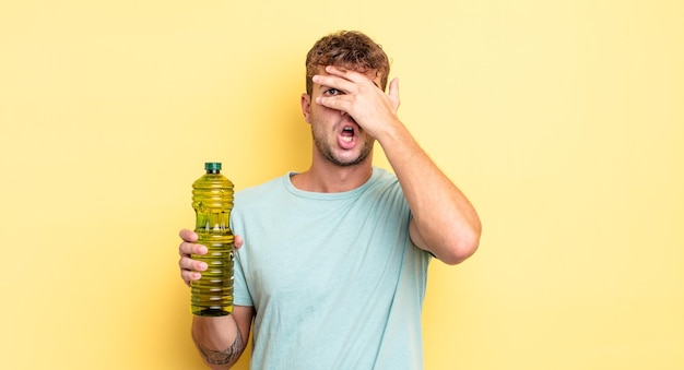 Jeune bel homme à l'air choqué, effrayé ou terrifié, couvrant le visage avec la main. notion d'huile d'olive