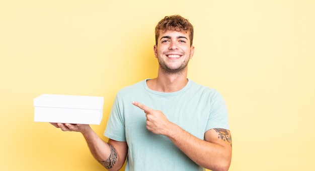 Jeune bel homme à l'air excité et surpris en pointant sur le côté. concept de boîte blanche