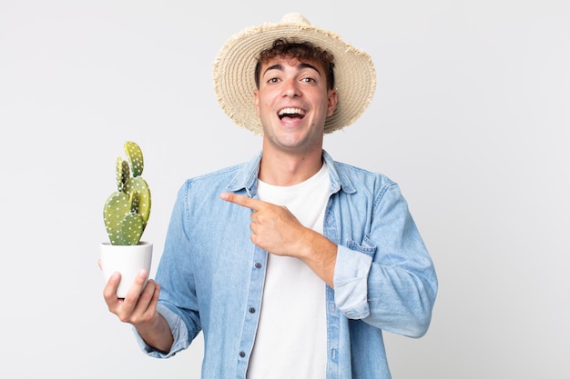 Jeune bel homme à l'air excité et surpris en pointant sur le côté. fermier tenant un cactus décoratif