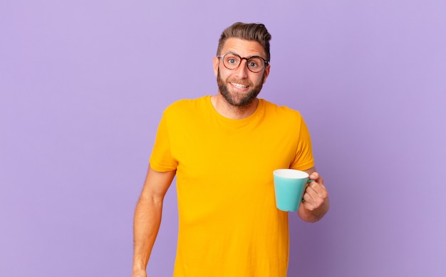 Jeune bel homme à l'air heureux et agréablement surpris. et tenant une tasse de café