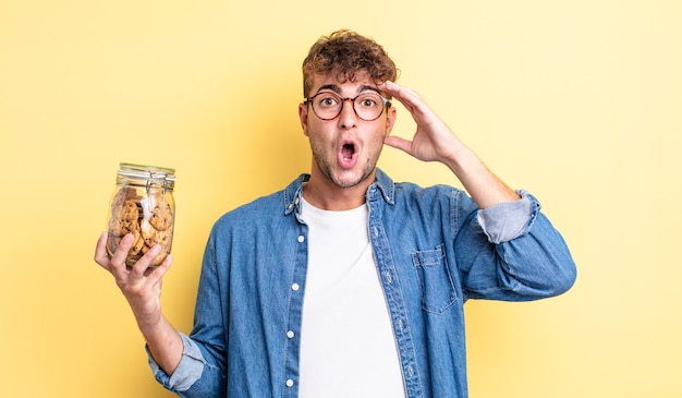 Jeune bel homme à l'air heureux, étonné et surpris. concept de bouteille de biscuits