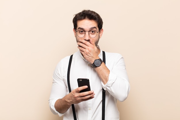 Jeune bel homme à l'air heureux, gai, chanceux et surpris couvrant la bouche avec les deux mains