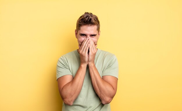 Jeune bel homme à l'air heureux joyeux chanceux et surpris couvrant la bouche avec les deux mains étrange concept de moustache