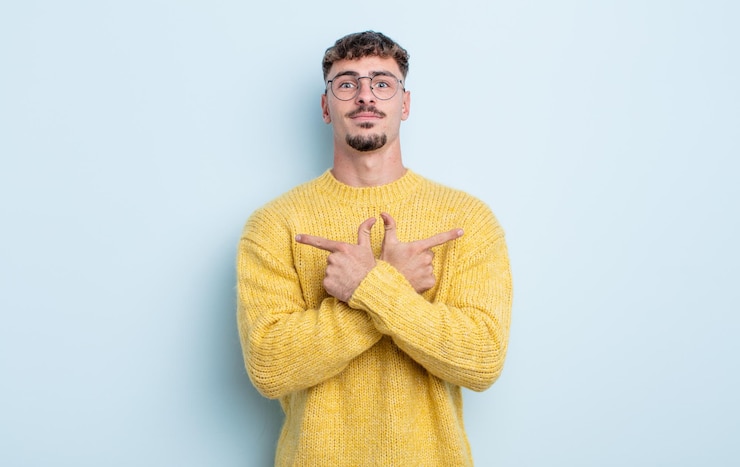 Photo jeune bel homme à l'air perplexe et confus, peu sûr et pointant dans des directions opposées avec des doutes