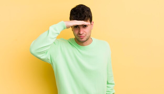 Jeune bel homme à l'air perplexe et étonné avec la main sur le front regardant au loin en regardant ou en cherchant