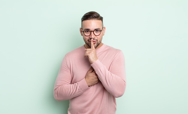 Jeune bel homme à l'air sérieux et croisé avec le doigt pressé sur les lèvres exigeant le silence ou le silence, gardant un secret