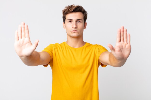 Jeune bel homme à l'air sérieux, malheureux, en colère et mécontent interdisant l'entrée ou disant stop avec les deux paumes ouvertes