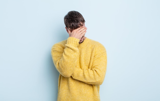 Jeune bel homme à l'air stressé, honteux ou contrarié, avec un mal de tête, couvrant le visage avec la main