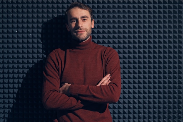 Jeune, bel homme appuyé contre un mur gris avec les bras croisés. Mâle souriant regardant la caméra.