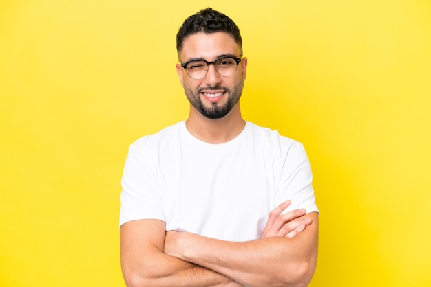 Jeune bel homme arabe isolé sur fond jaune avec des lunettes et une expression heureuse