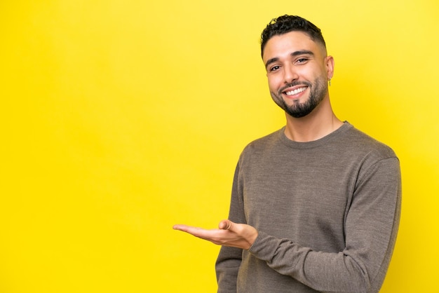 Jeune bel homme arabe isolé sur fond jaune présentant une idée tout en regardant en souriant vers