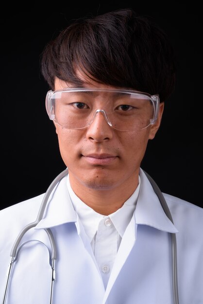 Jeune bel homme asiatique médecin portant des lunettes de protection sur fond noir