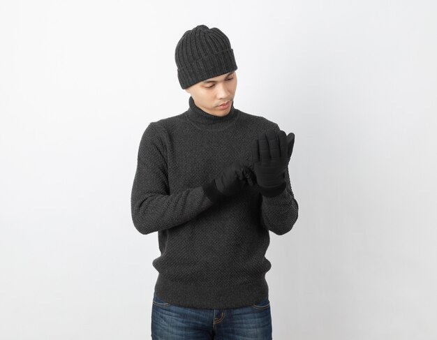 Jeune bel homme asiatique portant un pull gris, des gants et un bonnet à la recherche de ses gants chauds sur blanc