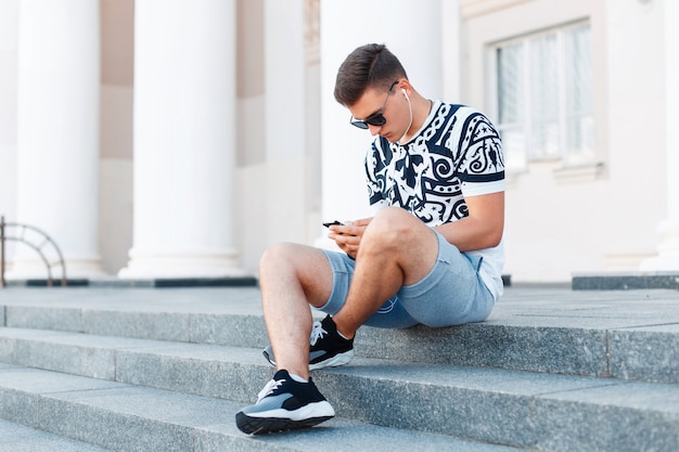 Jeune bel homme assis sur les marches et travailler sur votre téléphone.