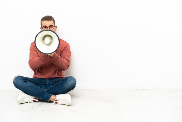 Jeune bel homme assis sur le sol en criant à travers un mégaphone