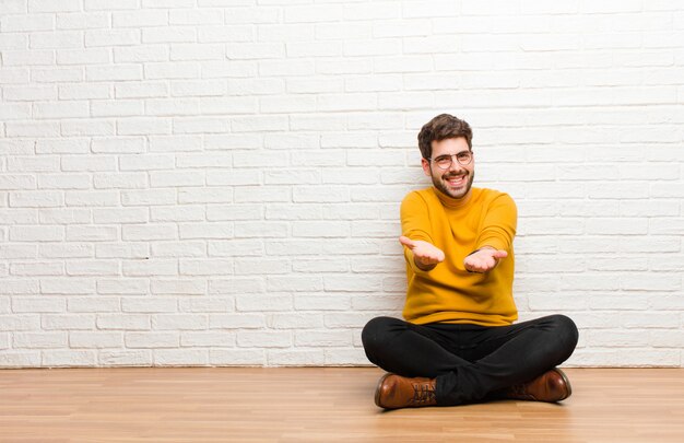 Jeune bel homme assis sur le sol de la maison contre la texture du mur de briques