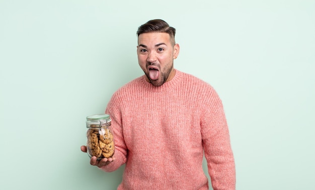 Jeune bel homme avec une attitude joyeuse et rebelle, plaisantant et tirant la langue. concept de bouteille de biscuits