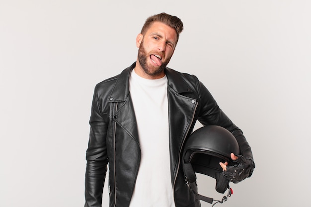 Jeune bel homme avec une attitude joyeuse et rebelle, plaisantant et tirant la langue. concept de casque de moto