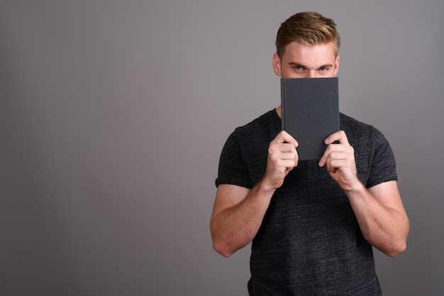 Jeune bel homme aux cheveux blonds portant une chemise grise sur un mur gris