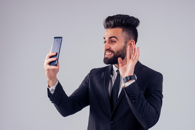 Jeune bel homme aux cheveux noirs en costume d'affaires élégant en studio isoler fond blanc vidéo chat en ligne distance sociale