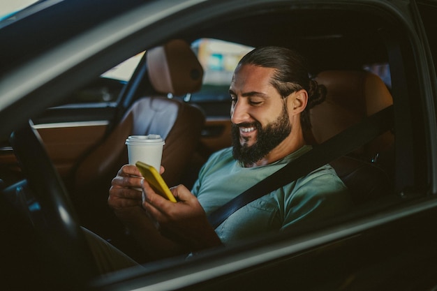 Jeune bel homme aux cheveux noirs tenant un téléphone et conduisant une voiture