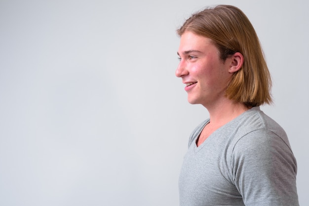 Jeune bel homme aux longs cheveux blonds contre le mur blanc