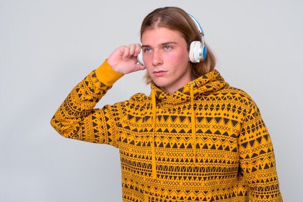 Jeune bel homme aux longs cheveux blonds contre le mur blanc