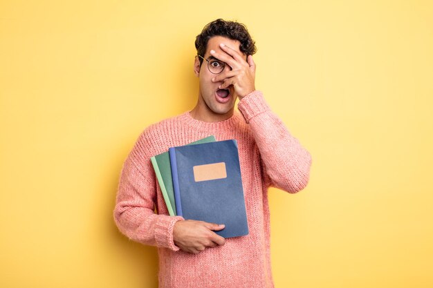 Jeune bel homme ayant l'air choqué, effrayé ou terrifié, couvrant le visage avec la main. concept de cahier