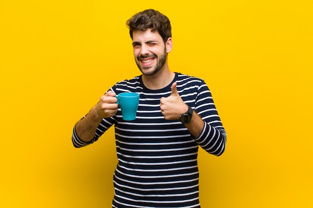 Jeune bel homme ayant un café contre le mur orange