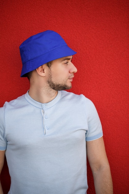 Photo jeune bel homme avec une barbe dans un chapeau panama sur la tête dans le contexte d'un mur rouge. portrait d'un mec en t-shirt blanc