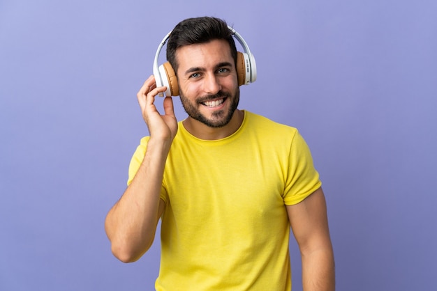 Jeune bel homme avec barbe isolé sur fond violet écouter de la musique