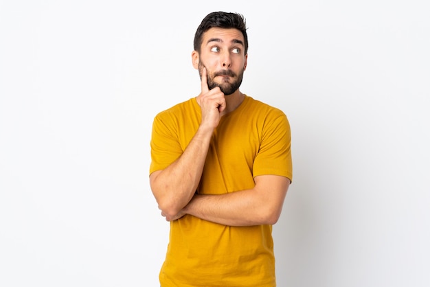 Jeune bel homme avec barbe isolé sur mur blanc ayant des doutes et de la pensée