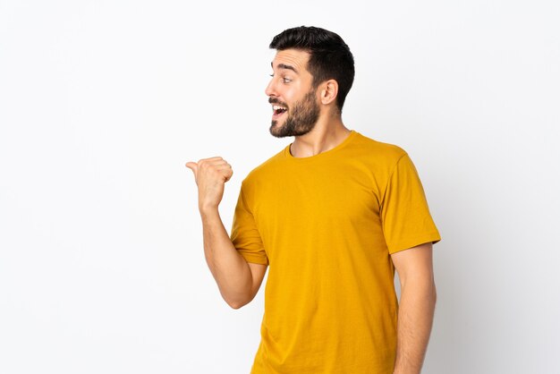 Jeune bel homme avec barbe isolé sur un mur blanc pointant vers le côté pour présenter un produit