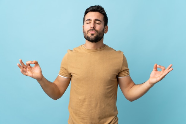 Jeune bel homme avec barbe sur mur isolé dans une pose zen