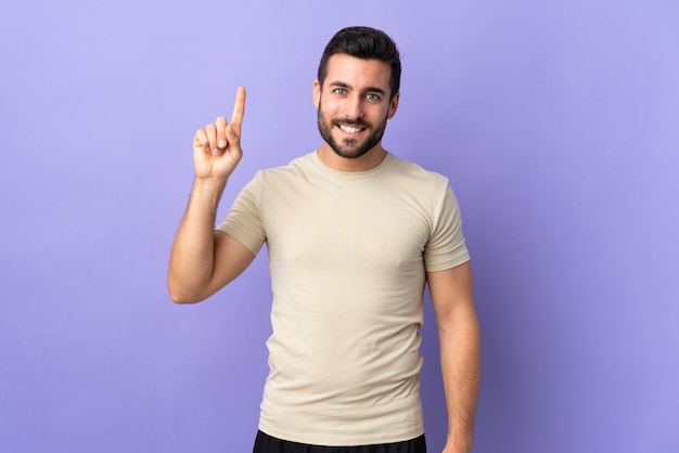 Jeune bel homme avec barbe sur mur isolé pointant vers le haut une excellente idée