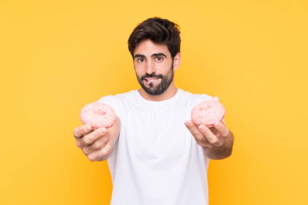 Jeune bel homme avec barbe sur mur jaune isolé tenant un beignet et triste