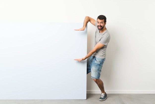 Jeune bel homme à la barbe tenant une grande pancarte vide bleue tenant la surface pour insérer une annonce