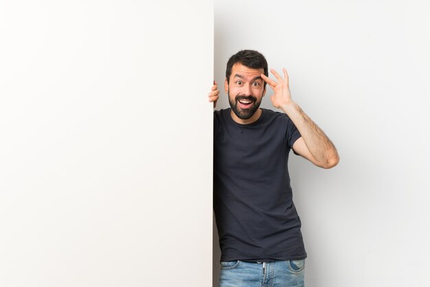 Jeune bel homme à la barbe tenant une grande pancarte vide vient de réaliser quelque chose et a l'intention de la solution